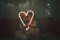 Kids in red hat holding big luminous heart formed with two candy sticks over dark background