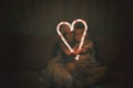 Kids in red hat holding big luminous heart formed with two candy sticks over dark background