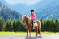 Kids riding pony. Child on horse in Alps mountains