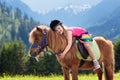 Kids riding pony. Child on horse in Alps mountains