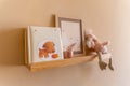 Kids room decor, wooden floating shelf interior child bedroom, empty wooden picture frame, books, poster blank canvas