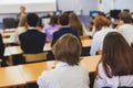 Kids in school writing and taking notes, teens pupils behind desks during the lesson listen to teacher lecture, classroom with Royalty Free Stock Photo