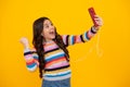 Kids selfie. Close-up portrait of cute teen girl using mobile phone, cell web app, isolated over bright vivid vibrant Royalty Free Stock Photo