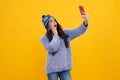Kids selfie. Close-up portrait of cute teen girl in winter knitted hat using mobile phone, cell web app,  over Royalty Free Stock Photo