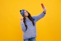 Kids selfie. Close-up portrait of cute teen girl in winter knitted hat using mobile phone, cell web app,  over Royalty Free Stock Photo