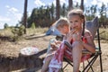 Kids sitting on touristic armchair, eating croissants and looking at sea during vacation at campsite