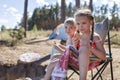 Kids sitting on touristic armchair, eating croissants and looking at sea during vacation at campsite