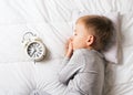 Kids sleeping concept with asleep little boy in bed with alarm clock