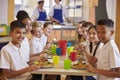 Kids at a table in a primary school cafeteria look to camera Royalty Free Stock Photo