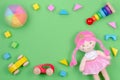 Kids toys background frame with toy doll, wooden cars and colorful blocks on green background