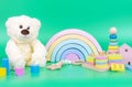 Kids toys collection. Teddy bear, wooden rainbow and baby educational toys on light green background