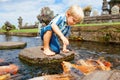 Kids walk by stepping stones, feeding koi fishes in pond