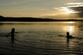 Kids in the water of a lake at sunset