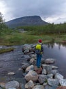 KilpisjÃÂ¤rvi, Finland - June 27, 2018: Man standing on top of rocks that go across a river, with Saana mountain in Lapland