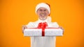 Kind aged man in santa claus hat showing gift box on camera and smiling surprise Royalty Free Stock Photo