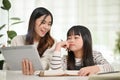 Kind Asian female sister teaching math to her little sister, looking at tablet screen together