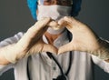 Kind elderly doctor in protective medical mask showing heart sign with hands in sterile gloves. The concept of a profession that Royalty Free Stock Photo