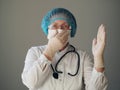 Kind elderly doctor in protective medical mask showing heart sign with hands in sterile gloves Royalty Free Stock Photo