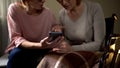 Kind female volunteer showing old woman in wheelchair how to use smartphone