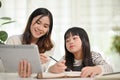 Kind and friendly Asian female sister teaching math to her little sister, looking at tablet screen