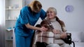 Kind nurse covering with blanket handicapped old woman, hospital care, service