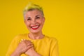 Kind positive mature woman with colored stylish yellow dyed hair in warm dress and make up red lipstick on lips amazed