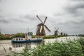 Straight canal with tall bushes, windmills and boat at Kinderdijk. Royalty Free Stock Photo