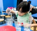 Kindergarten girl pouring clear solution into a cup on blue table.