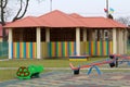 Kindergarten playground with bright new alcove with multicolored low fence, funny bench and seesaw swing in big yard with soft