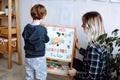 Kindergartener stand with back and learn english letters, alphabet and numbers on magnetic board. Educator sit near boy