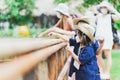 A kindergartener wearing a white face mask in a 4D shape is feeding the fish, the child stands behind a bamboo fence for safety