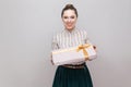 Kindness attractive young adult woman in white with green lines skirt standing and giving you present with yellow bow and toothy Royalty Free Stock Photo