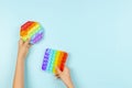 Kids hands holding colorful pop it fidget toys on blue background. Push pop-it fidgeting game for children
