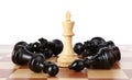 King among fallen black chess pieces on wooden board against white background Royalty Free Stock Photo