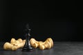 King among fallen chess pieces on black table against dark background. Space for text