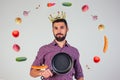 King of the kitchen with a golden crown on head chef holding a frying pan wizard man is cooking magic flying food salad