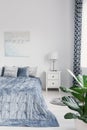 King size bed with elegant blue bedding, white nightstand with lamp and painting on the wall in luxury bedroom interior, real phot Royalty Free Stock Photo