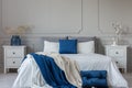 King size bed with grey, blue and white bedding between two wooden nightstands with flowers in vases Royalty Free Stock Photo