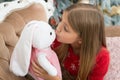 A kissable cutie. Small girl kiss rabbit toy. Little girl with cute bunny at Christmas tree. Little child play with soft