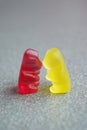 Kissing gummy bears, yellow and red, on a grey background, funny love