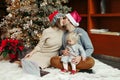 Kissing mother and father in Santa hats with baby girl calling family friends on a video call. Distant remote holiday celebration Royalty Free Stock Photo