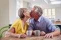 Kissing Retired Couple Sitting Around Table At Home Having Morning Coffee Together Royalty Free Stock Photo