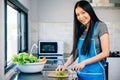 An unrecognizable woman in a blue apron prepares a nutritious dinner cutting