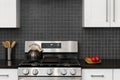 A kitchen detail with white cabinets and a black square tile backsplash.