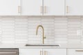 A kitchen detail with white cabinets, gold faucet, and tiled backsplash.