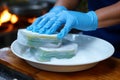 Kitchen duty closeup Hand in blue gloves uses a sponge for dish cleaning