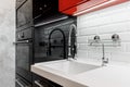 Kitchen faucet is black, near the wall with glossy white bricks and glossy black and red cabinets Royalty Free Stock Photo