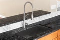 A kitchen faucet detail with a black marble countertop and herringbone backsplash.