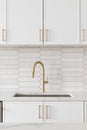 A kitchen faucet detail with a gold faucet, brown backsplash, and white cabinets. Royalty Free Stock Photo