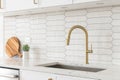 A kitchen faucet detail with a gold faucet, brown backsplash, and white cabinets. Royalty Free Stock Photo